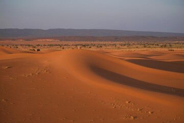 Dunes of Sahara in sunset light with little silhouettes of people. Morocco