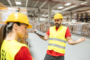 A man is engaging with a female colleague in a warehouse, discussing work-related matters while surrounded by packages.