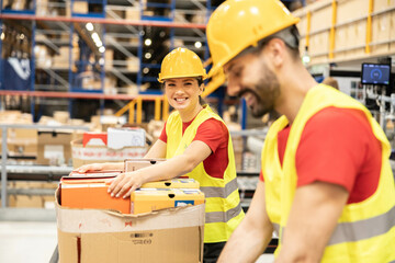 Two colleagues in a warehouse smile while sorting through packages, showcasing a positive work...