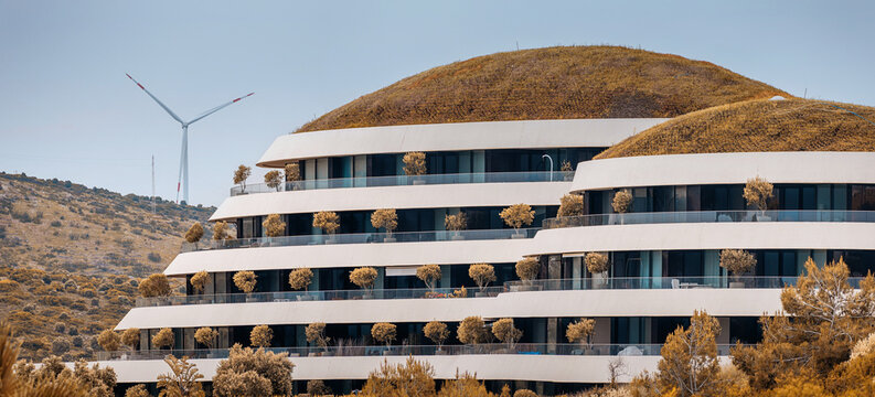 28 April 2025, Cesme, Turkiye: White modern building with green roof promoting sustainable architecture and renewable energy with wind turbine
