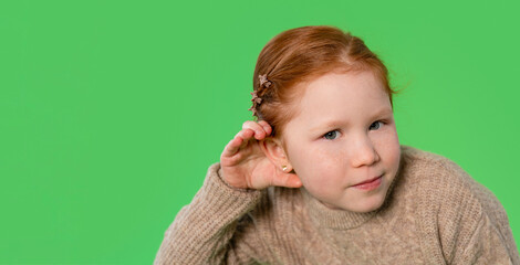 Young girl with red hair listens intently while wearing a cozy sweater against a vibrant green...