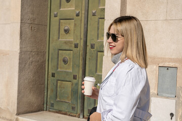 Smiling female doctor wearing sunglasses and holding coffee outside hospital