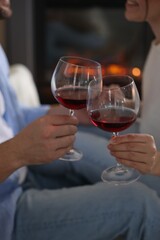 Couple clinking glasses of wine near fireplace at home, selective focus