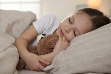 Cute girl with teddy bear sleeping in bed at home