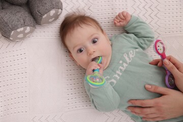 Mother and her cute little baby with rattle toy on bed at home, above view