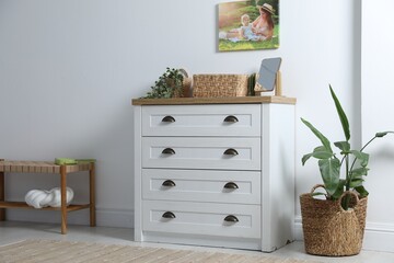 Dresser with stylish decor and houseplants near white wall indoors