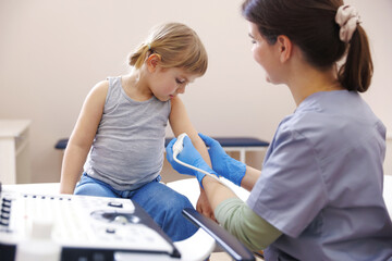 Sonographer conducting ultrasound examination of little girl's arm in clinic