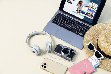 Laptop with travel blog web site and different stuff on beige background, above view. Space for text