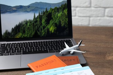 Passports, flight tickets, plane model and laptop on wooden table, closeup