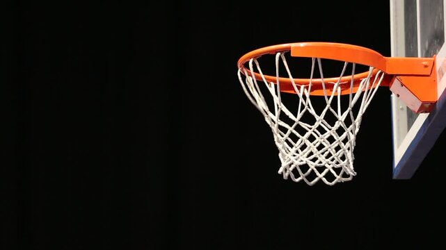 Close-up of a basketball swishing perfectly through an orange hoop and white net. Dynamic sports action shot isolated on a stark black background, highlighting success.
