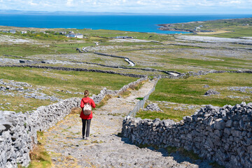 A tourist walking a trail on Inishmore with endless stone walls and the vast Atlantic stretching to the horizon.
