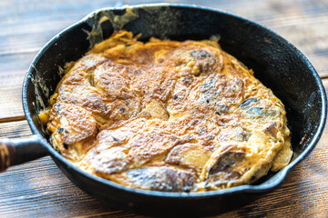 Traditional spanish breakfast potato tortilla. Potatoes in a cast iron frying pan on a rustic wooden background.