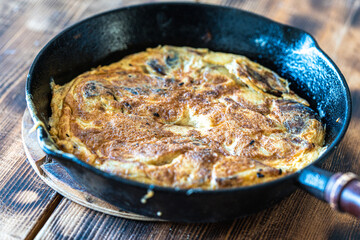 Traditional spanish breakfast potato tortilla. Potatoes in a cast iron frying pan on a rustic wooden background.