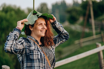 A woman holds a large burdock leaf in her hand. A woman plays with a huge sheet.