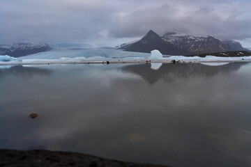 Glacier lagoon reflecting mountains under cloudy sky in iceland