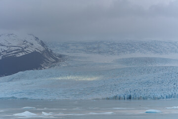 Glacier lagoon reflecting cloudy sky with floating icebergs in Iceland