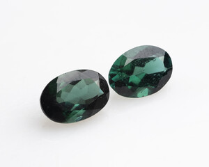 Pair of Natural Chrome Tourmaline gemstones, oval-shaped, displaying a deep forest green hue with subtle variations and internal inclusions, resting on a white background