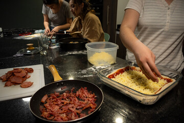 Three unrecognizable women collaborate in a kitchen, making pizza, food using dough and molds