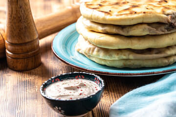Khychins, traditional Caucasian, Eastern dish. Flatbread stuffed with minced meat with sauce on a turquoise plate with cutlery and a napkin on a wooden table. Close-up.