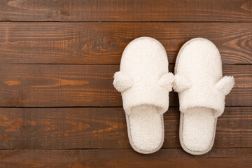 Soft teddy slippers on wooden background, top view