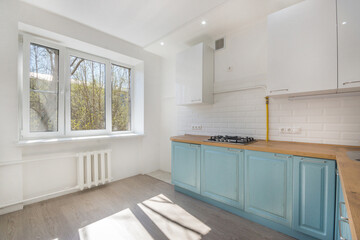 Bright kitchen with installed cabinet furniture. Laminated floor. An empty room, unfurnished.