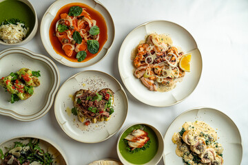 A colorful array of gourmet dishes is beautifully presented on a white tablecloth, featuring fresh seafood, vibrant vegetables, and herbs, showcasing the artistry of culinary delight
