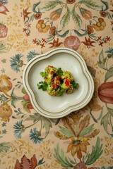 A beautifully arranged dish showcases a variety of colors and textures, featuring fresh ingredients and artistic garnishes on an ornate tablecloth, elevating the dining experience