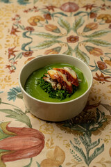 Delight in a beautifully crafted dish showcasing a creamy green puree adorned with tender grilled chicken, presented on an artistically patterned tablecloth in an inviting restaurant ambiance