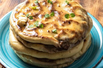 Khychins, traditional Caucasian, Eastern dish. Flatbread stuffed with minced meat with sauce on a turquoise plate with cutlery and a napkin on a wooden table. Close-up.