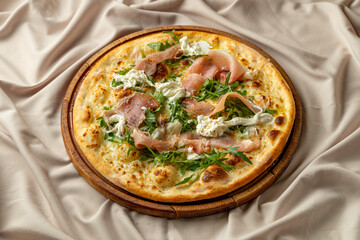 Vibrant pizza garnished with prosciutto, creamy cheese, and arugula rests on a wooden board, inviting patrons to savor the flavors in a cozy dining atmosphere