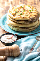 Khychins, traditional Caucasian, Eastern dish. Flatbread stuffed with minced meat with sauce on a turquoise plate with cutlery and a napkin on a wooden table. Vertical photo.
