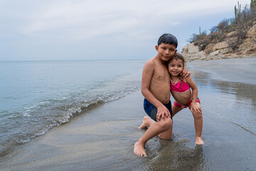 Latino brother and sister hugging on a Colombian beach on a cloudy day