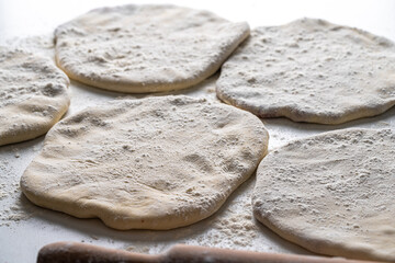 Raw Khychins, traditional Caucasian, Eastern dish. Flatbread stuffed with minced meat on a white table with flour and a rolling pin. Ready to fry.