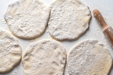 Raw Khychins, traditional Caucasian, Eastern dish. Flatbread stuffed with minced meat on a white table with flour and a rolling pin. Ready to fry.