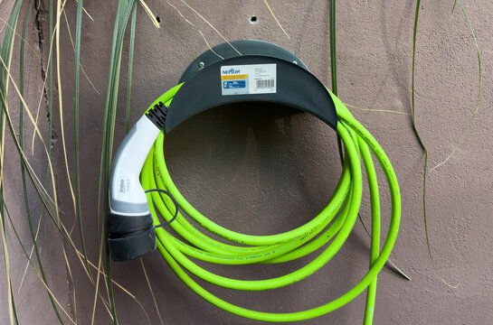 Paris, France - May 12, 2025: A bright green electric vehicle charging cable with a Type 2 Valeo connector is neatly wrapped and mounted on a Neptun wall holder attached to a textured exterior wall