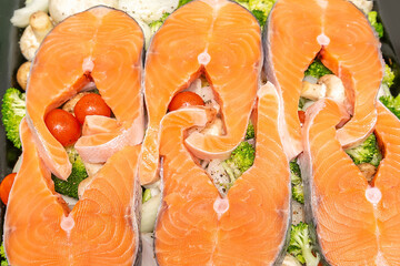 Raw fresh cut salmon fish steak slices on tomatoes,champignons mushrooms,broccoli vegetables, organic sea bass preparing for cooking,baking in stove.healthy diet food.