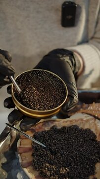 Chef holding open tin of black caviar over scallop shell