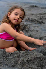 Latina girl in a pink swimsuit playing with sand on the beach