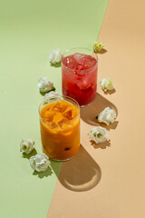 Two colorful, refreshing non-alcoholic drinks sit elegantly on a pastel background, surrounded by...