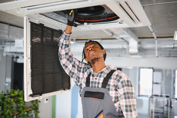 Technician repairing air conditioning ventilation system in office building