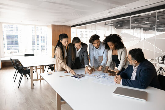 Five serious professionals, team members gather around conference table, review papers document, engaged in collaboration, problem-solving in modern office. Teamwork, data analysis, project planning