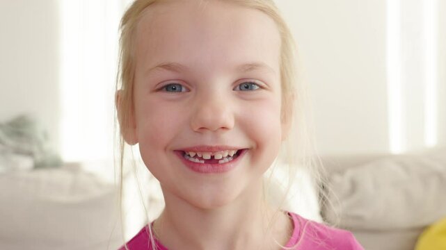Joyful moments of a young girl celebrating her lost milk tooth with a big toothless smile while enjoying a sunny day indoors
