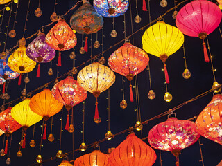 Many beautiful colorful Chinese lanterns hang in the dark night, lighting the street.