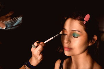 Obraz premium Woman being made up with eye shadow in a dark, elegant, baroque style environment