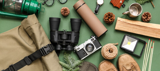 Composition with different travel items, shoes, thermos and pine cones on green background