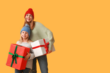 Cute little girl and her mother with Christmas gift boxes on yellow background