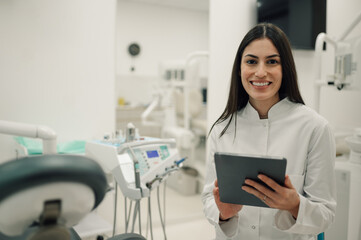 Dentist smiling and holding tablet in dental clinic
