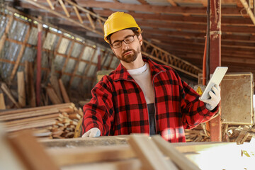 Male carpenter with tablet computer working at sawmill
