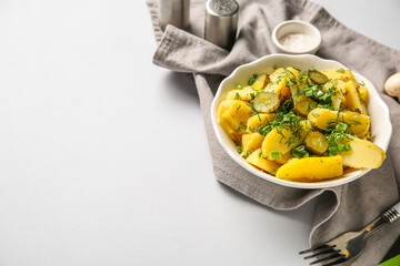 Bowl of tasty potato salad with green onion and pickled cucumber on grey background