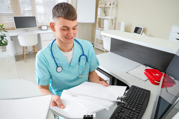 Male medical intern with papers at reception desk in clinic